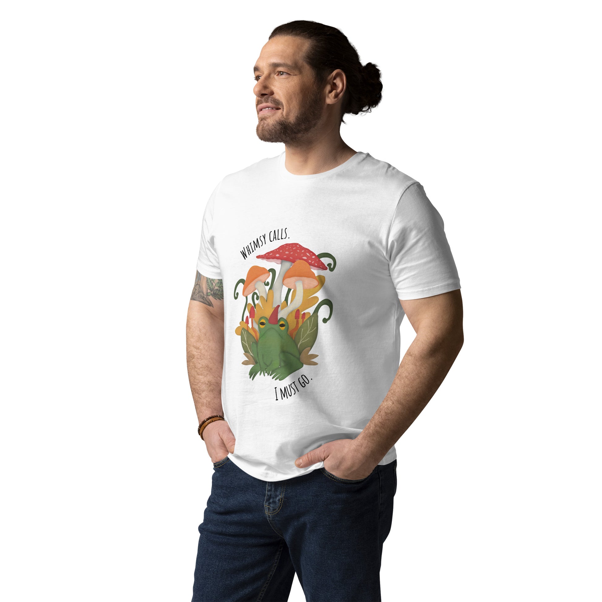 Person wearing a white graphic t-shirt  with an illustrated design of a frog amongst mushrooms and leaves. Words on the t-shirt read whimsy calls I must go